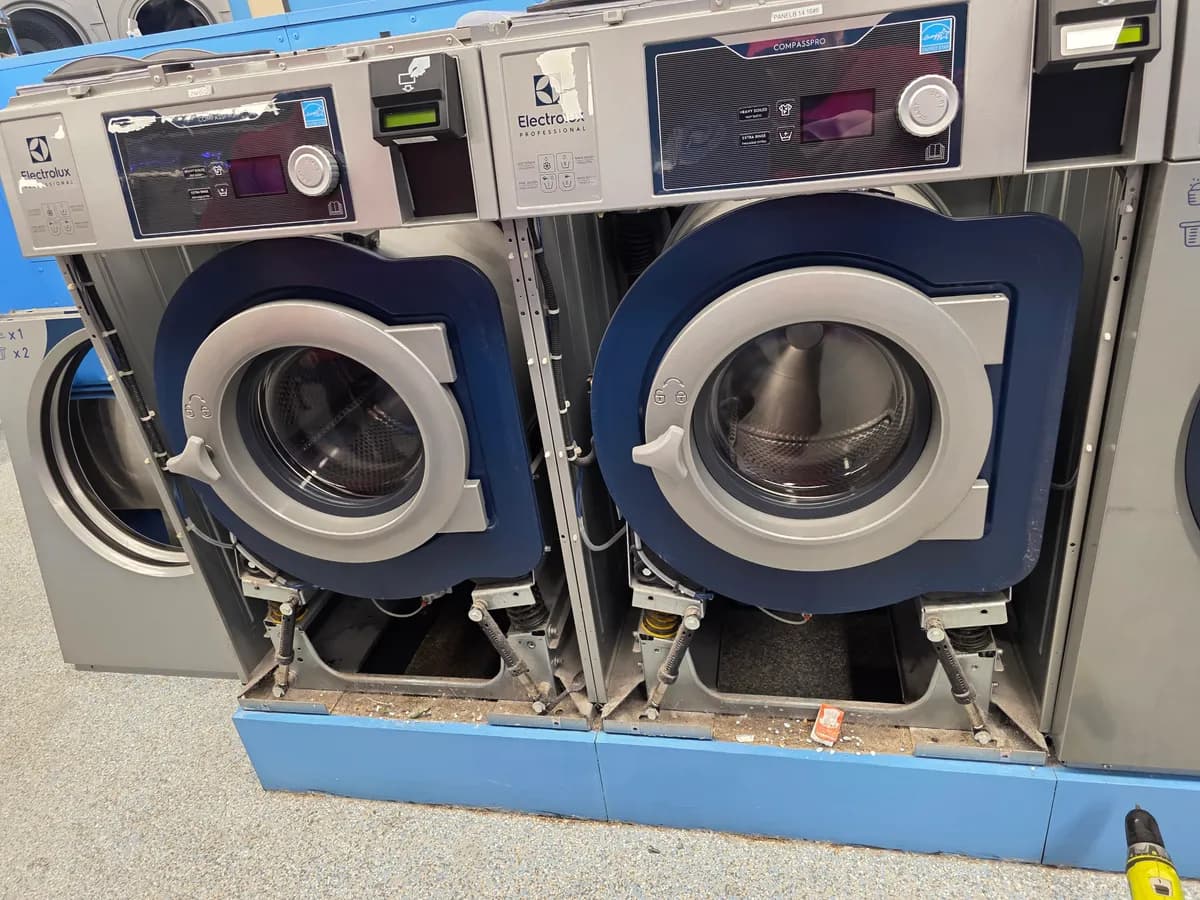 Two commercial washers with their front panels removed for repair