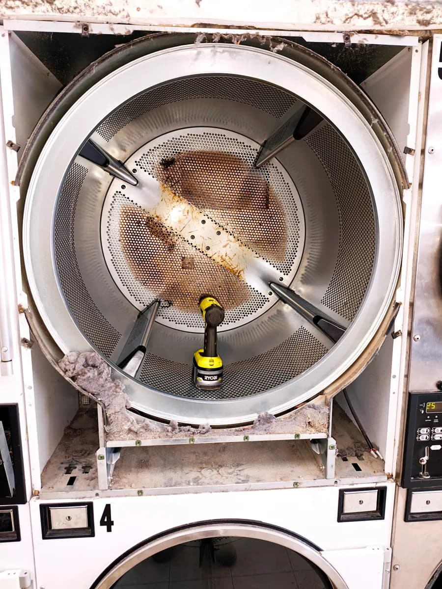 Commercial dryer with the front removed, showing a lint-covered drum during repair